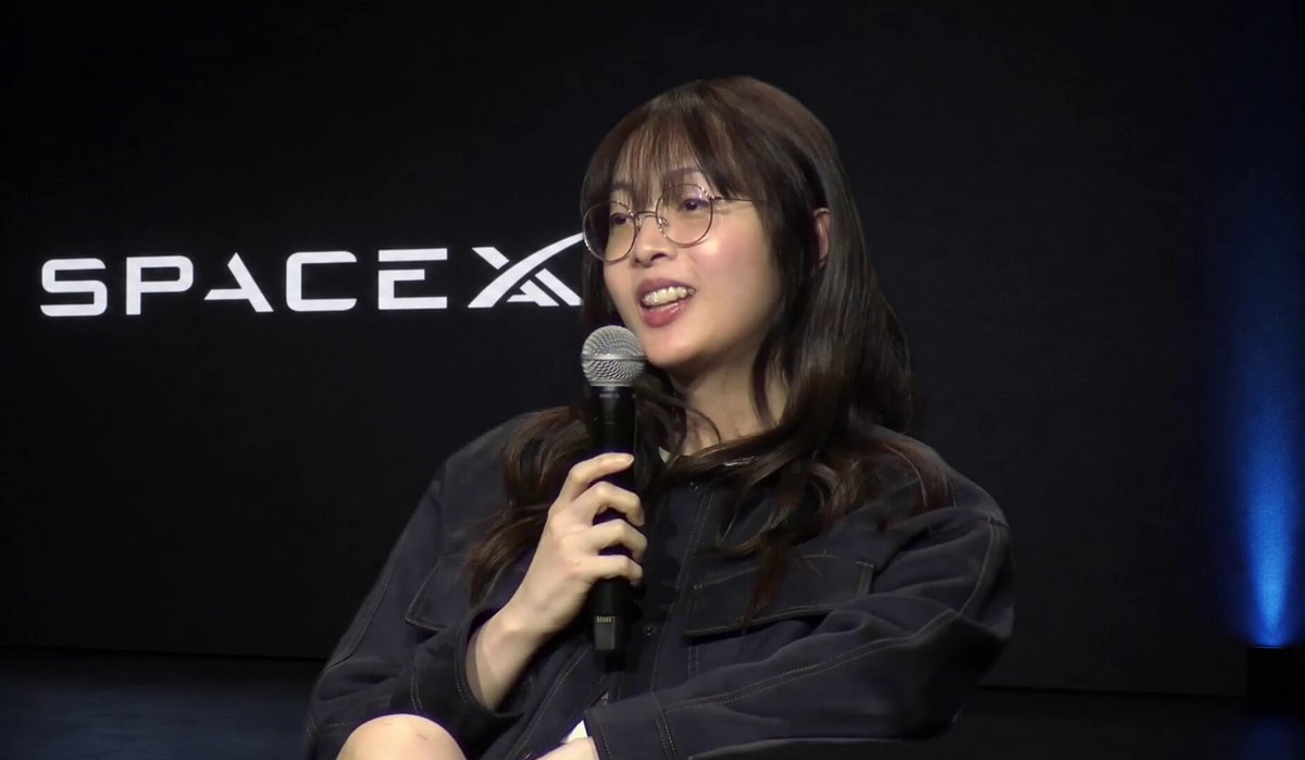 SPACEX 백드롭 앞에서 마이크를 들고 말하는 발표자