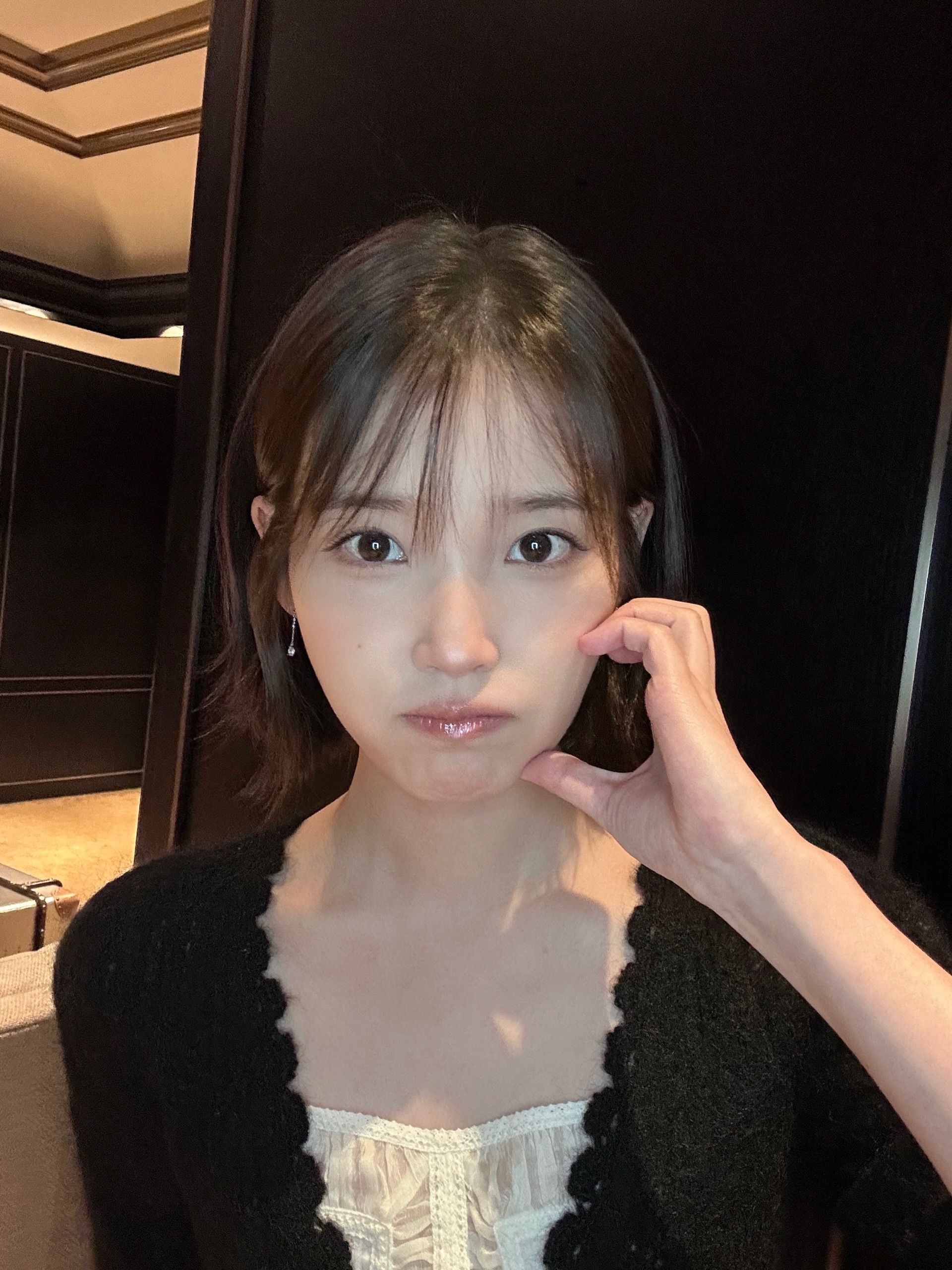 검은 겉옷 차림의 인물이 볼 옆에 손을 댄 근접 사진