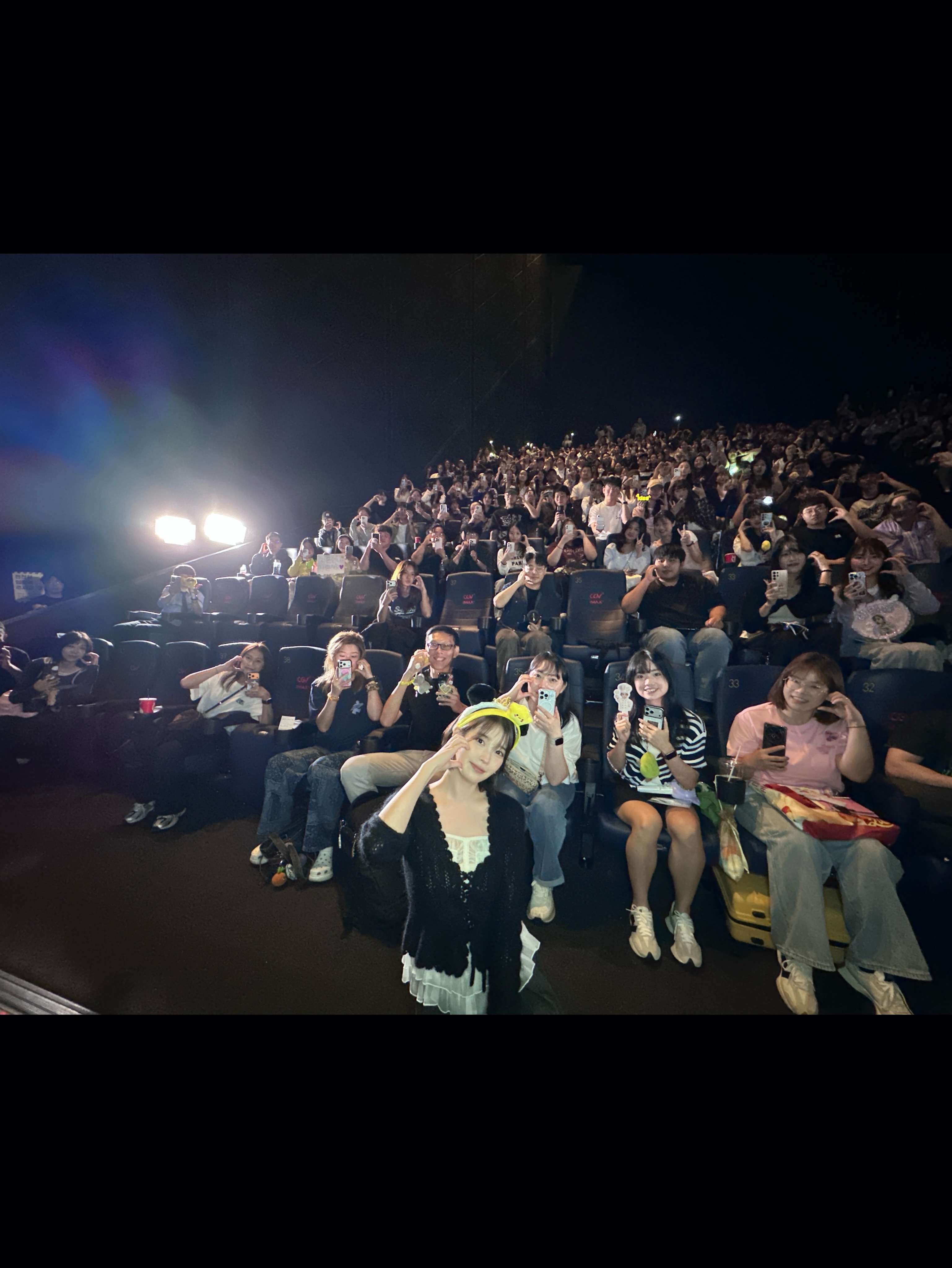 인물 뒤로 여러 줄의 관객석과 관객들이 보이는 사진